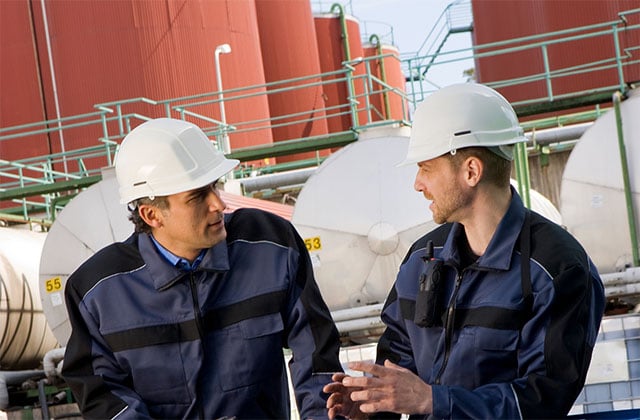Two-energy-workers-discuss-in-front-of-oil-tanks-640x420