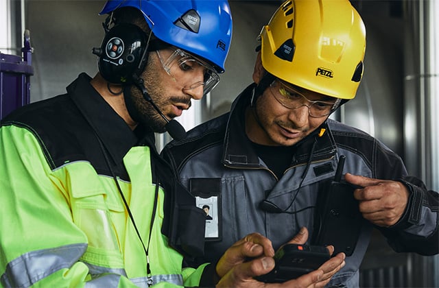 Two men in helmets look at a smart device