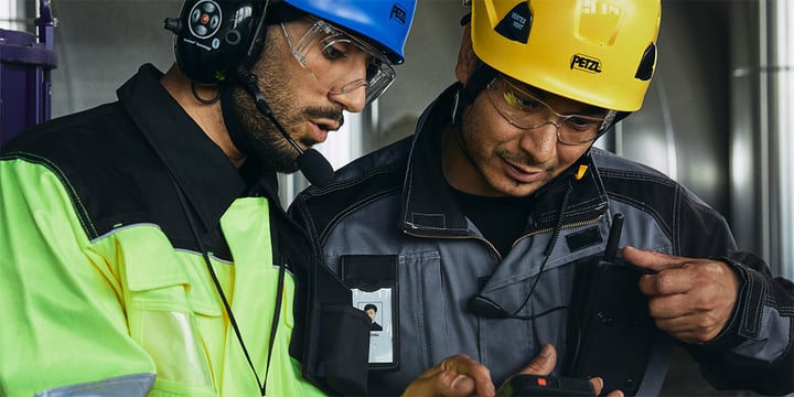 Two men in helmets, looking at a hybrid smart device