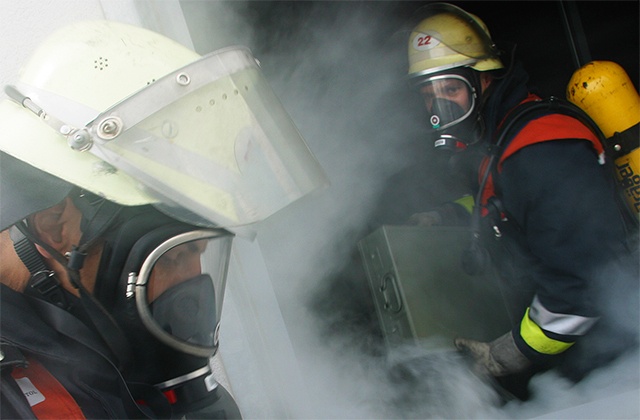 Two firemen working in smoke, wearing gas masks